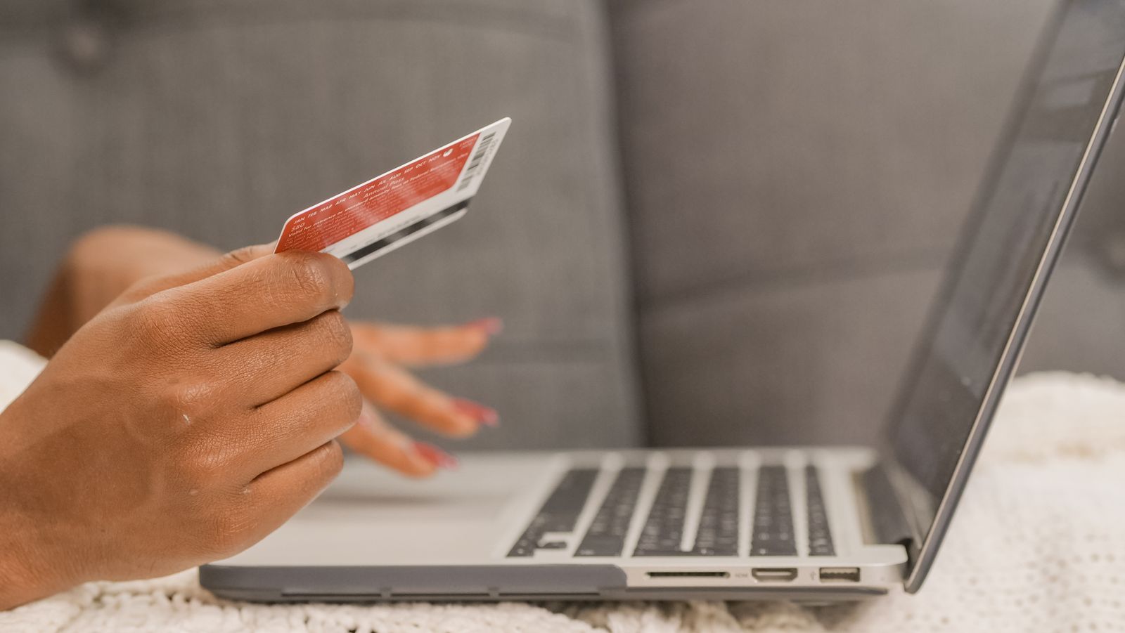 A hand holding a payment card next to an open laptop