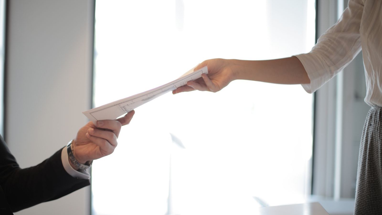 One person handing a printed document across a desk to another