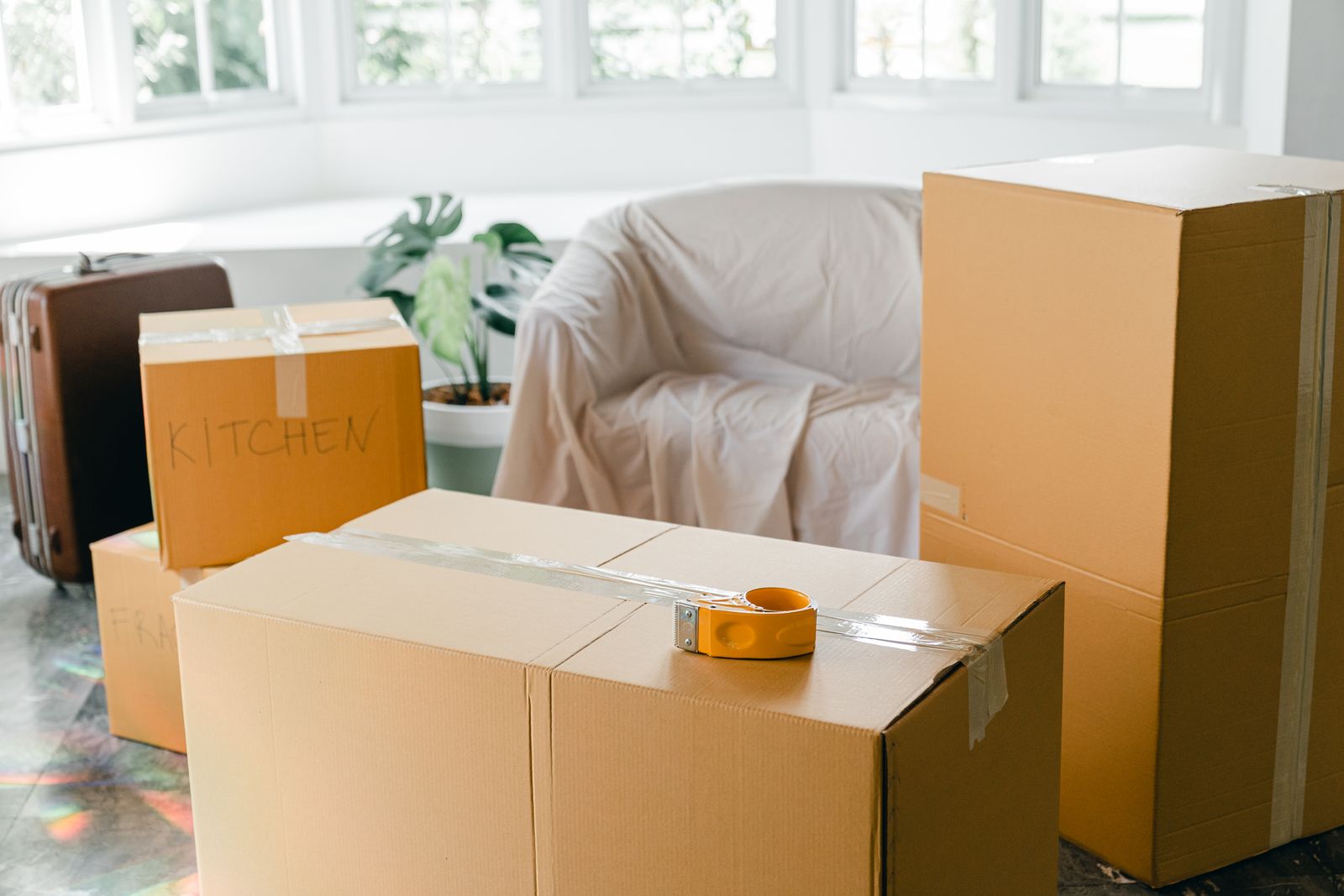 Packed and taped cardboard moving boxes in a bright room, one labelled kitchen