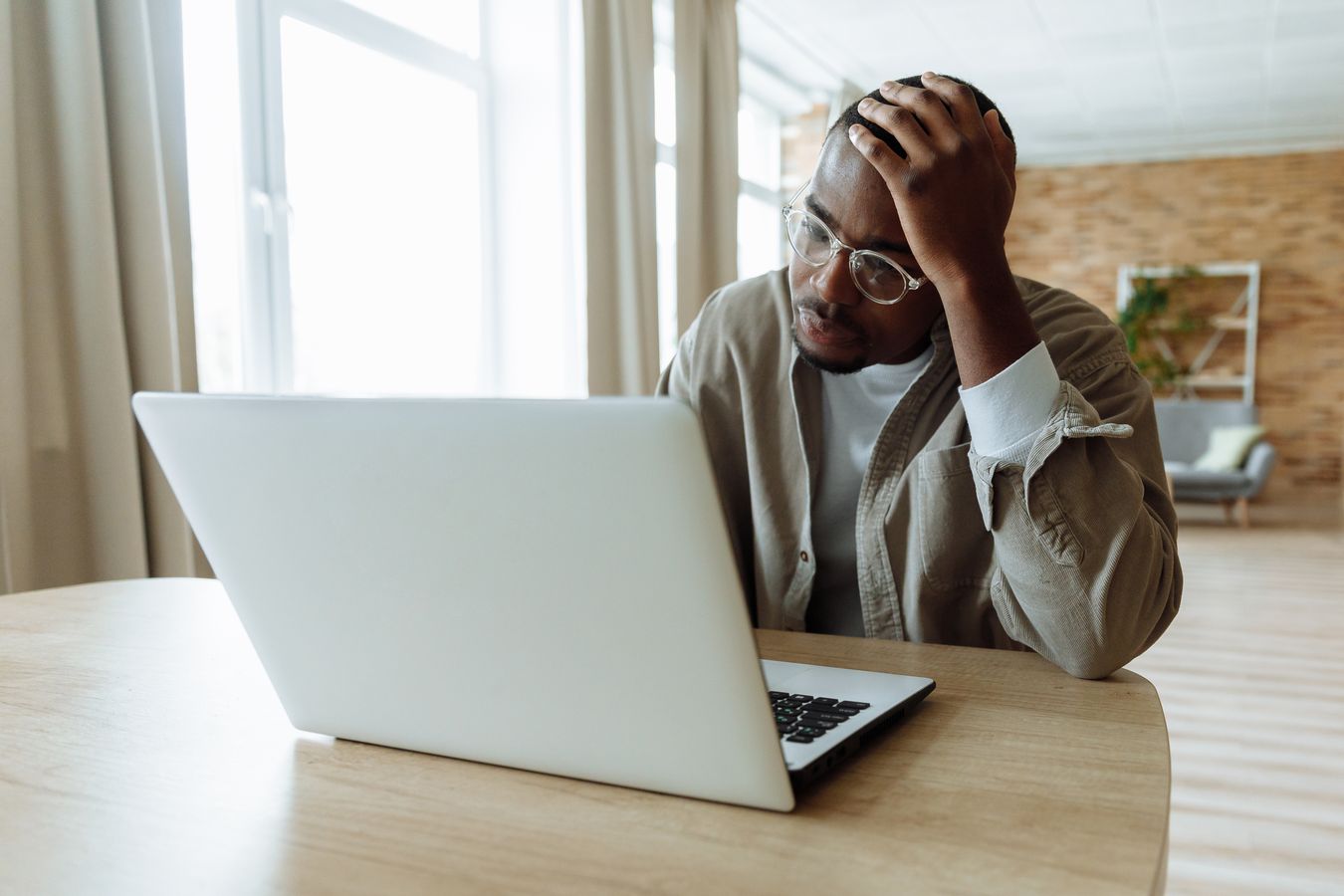 A man at a wooden desk holding his head with one hand as he stares at an open laptop