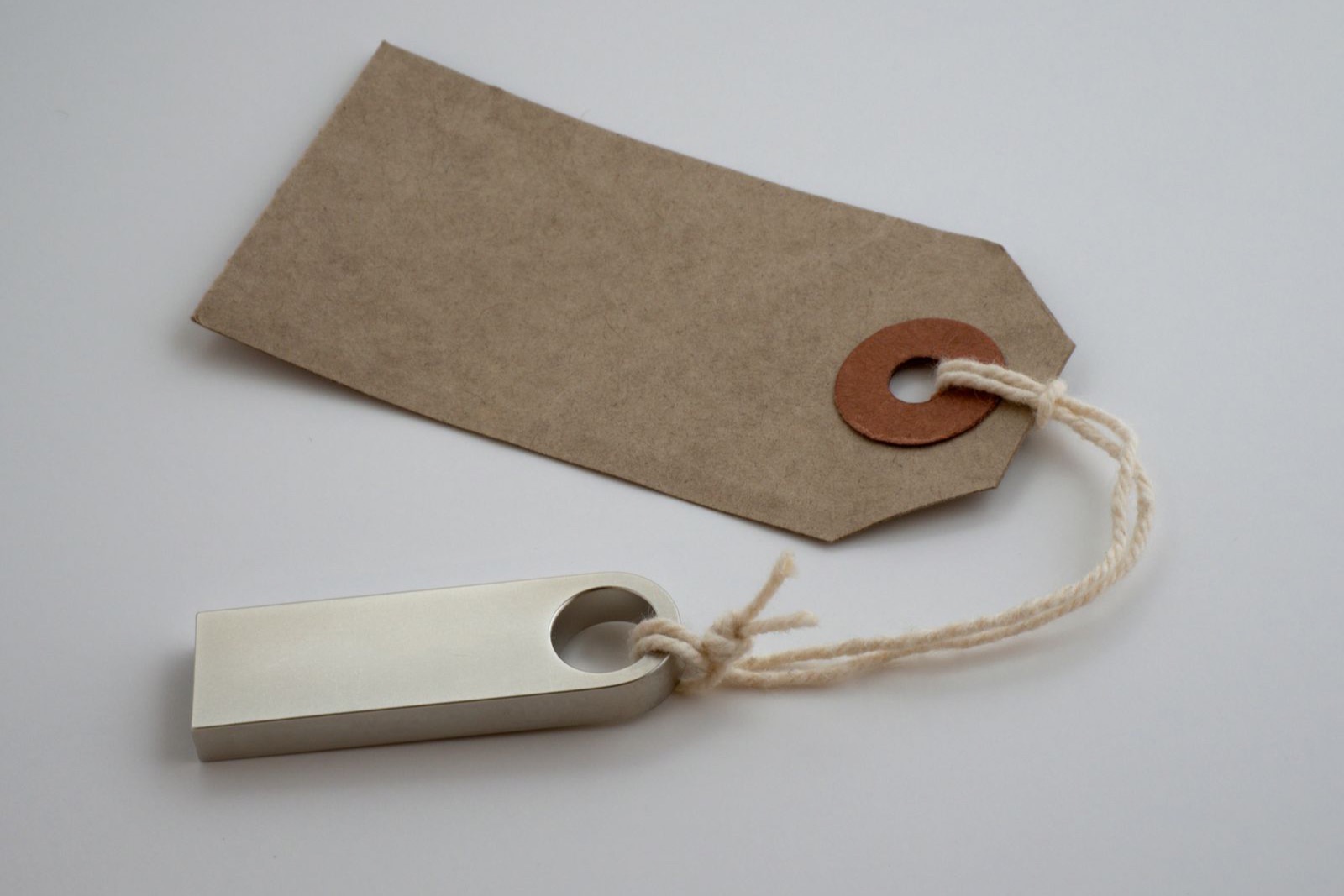 A blank brown paper price tag tied with string to a silver USB stick on a grey surface