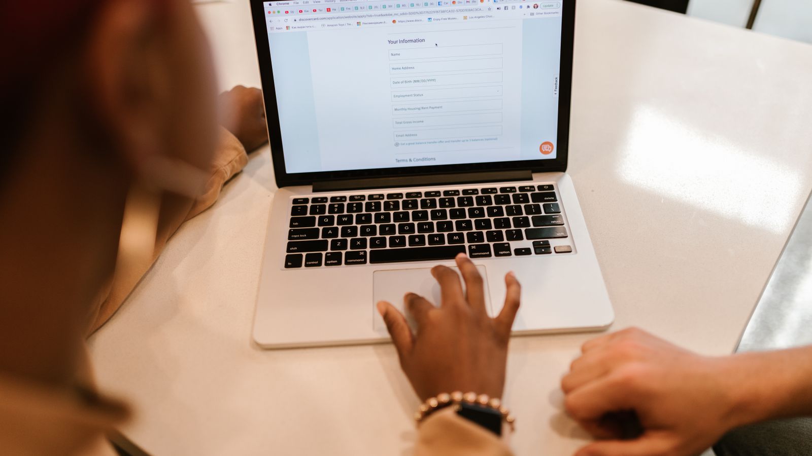 Two people at a table filling in a long online form on a laptop